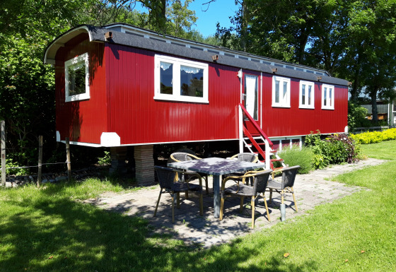 Lodge Pipowagen rojo en Camping De Gouwe Stek, Países Bajos, rodeado de árboles y área de jardín.