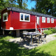 Rød Pipowagen-lodge ved Camping De Gouwe Stek i Holland, omgivet af grønne træer og havebord.