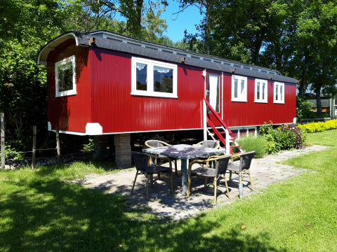 Lodge Pipowagen rojo en Camping De Gouwe Stek, Países Bajos, rodeado de árboles y área de jardín.