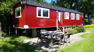 Lodge Pipowagen rojo en Camping De Gouwe Stek, Países Bajos, rodeado de árboles y área de jardín.