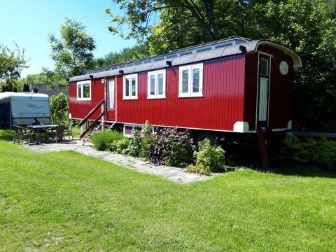 Cabaña roja llamada Pipowagen Snuf en Camping De Gouwe Stek, Países Bajos, rodeada de césped verde.