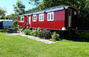 Cabaña roja llamada Pipowagen Snuf en Camping De Gouwe Stek, Países Bajos, rodeada de césped verde.