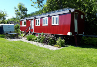 Cabaña roja llamada Pipowagen Snuf en Camping De Gouwe Stek, Países Bajos, rodeada de césped verde.