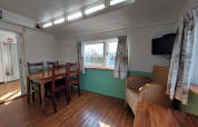 Interior de Pipowagen Snuf en Camping De Gouwe Stek, Países Bajos, con mesa de comedor y silla de mimbre.