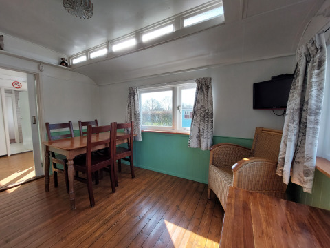 Interior de Pipowagen Snuf en Camping De Gouwe Stek, Países Bajos, con mesa de comedor y silla de mimbre.