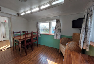 Interior de Pipowagen Snuf en Camping De Gouwe Stek, Países Bajos, con mesa de comedor y silla de mimbre.