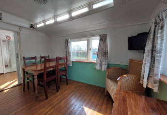 Interior de Pipowagen Snuf en Camping De Gouwe Stek, Países Bajos, con mesa de comedor y silla de mimbre.