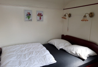 Habitación acogedora con cama, dos almohadas, lámparas de pared y cuadros de flores sobre la cama.