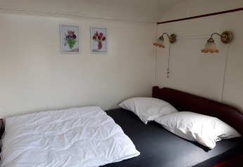 Habitación acogedora con cama, dos almohadas, lámparas de pared y cuadros de flores sobre la cama.