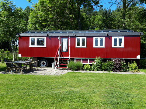 Pipowagen Snuf rojo en Camping De Gouwe Stek, Países Bajos, rodeado de césped, árboles y muebles de exterior.