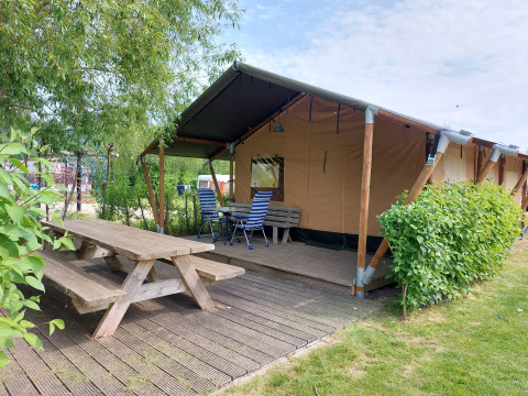 Tienda safari Glamping Ekster en Camping De Gouwe Stek, Países Bajos, con terraza de madera y bancos.