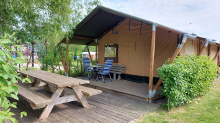 Tienda safari Glamping Ekster en Camping De Gouwe Stek, Países Bajos, con terraza de madera y bancos.