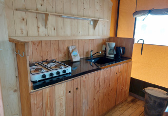Área de cocina en una tienda safari glamping con estufa, fregadero y cafetera en Camping De Gouwe Stek.