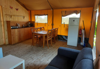 Interior de la tienda Glamping Safari Ekster con cocina, mesa de comedor, sofá y nevera en Camping De Gouwe Stek.