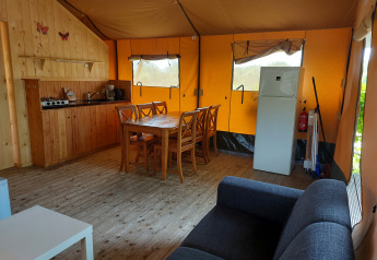 Interior de la tienda Glamping Safari Ekster con cocina, mesa de comedor, sofá y nevera en Camping De Gouwe Stek.