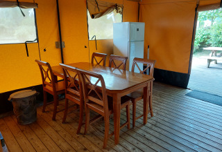 Interior de una tienda de safari glamping con mesa, sillas y nevera en Camping De Gouwe Stek, Países Bajos.