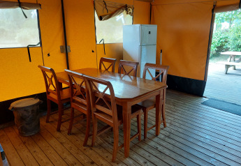 Interior de una tienda de safari glamping con mesa, sillas y nevera en Camping De Gouwe Stek, Países Bajos.