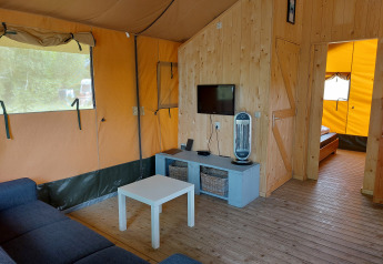 Vista interior de la Glamping Safari tent Ekster en Camping De Gouwe Stek, con sofá, mesa, TV y paneles de madera.