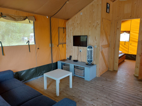 Indretning af en komfortabel safariteltsuite med sofa, bord, tv og træpaneler på Camping De Gouwe Stek.