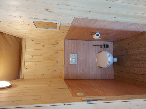 Baño con paneles de madera, inodoro, escobilla y papel en la tienda Glamping Safari Ekster, Países Bajos.