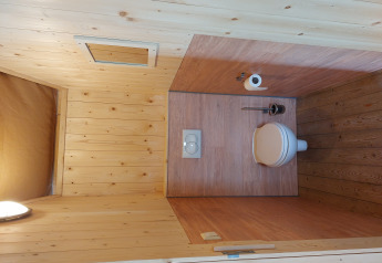 Baño con paneles de madera, inodoro, escobilla y papel en la tienda Glamping Safari Ekster, Países Bajos.