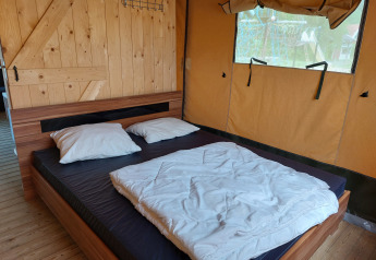 Vista interior de una tienda safari con cama doble y pared de madera en Camping De Gouwe Stek, Países Bajos.