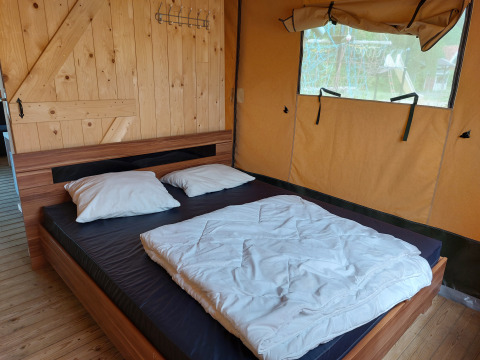 Vista interior de una tienda safari con cama doble y pared de madera en Camping De Gouwe Stek, Países Bajos.