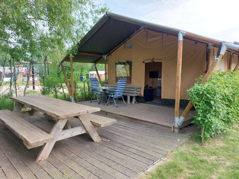 Tienda safari con terraza y asientos al aire libre en Camping De Gouwe Stek, rodeada de naturaleza en Holanda.