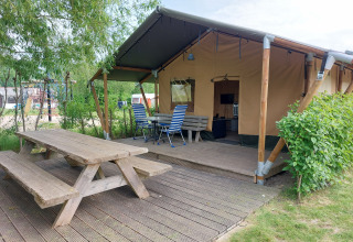 Tienda safari con terraza y asientos al aire libre en Camping De Gouwe Stek, rodeada de naturaleza en Holanda.