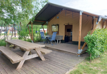 Tienda safari con terraza y asientos al aire libre en Camping De Gouwe Stek, rodeada de naturaleza en Holanda.