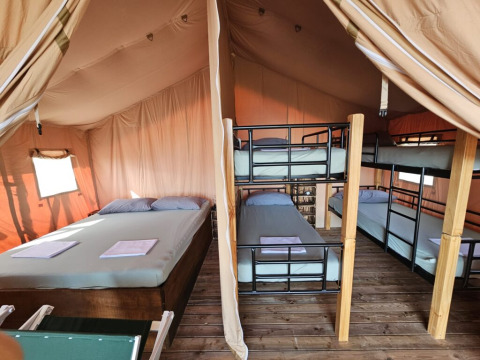 Interior de tienda safari con cama doble y literas en Agricola La Casetta, Italia, suelo de madera visible.