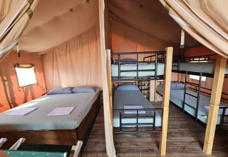 Interior de tienda safari con cama doble y literas en Agricola La Casetta, Italia, suelo de madera visible.