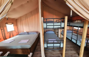 Safari tent interior with a double bed and bunk beds at Agricola La Casetta in Italy, wooden floor visible.