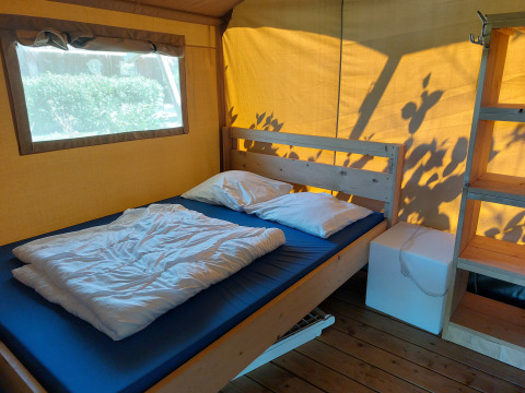 Habitación de lodge interior con cama doble, cojines blancos, estantería de madera y ventana amplia.