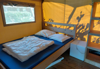 Interior photo of a lodge room with double bed, white pillows and bedding, wooden shelving and window.