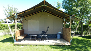 Safari tent lodge at Camping De Gouwe Stek in the Netherlands, featuring a porch with seating and chairs.