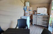 Interior of a lodge featuring a small kitchen area, table, chairs, fridge, and gas stove on wood floor.