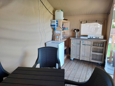 Interior of a lodge featuring a small kitchen area, table, chairs, fridge, and gas stove on wood floor.