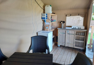 Interior de un lodge con cocina pequeña, mesa, sillas, nevera y hornillo sobre suelo de madera.