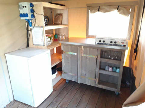 Pequeña cocina con estufa, nevera y estantes abiertos en la Safari tent Merel de Camping De Gouwe Stek.