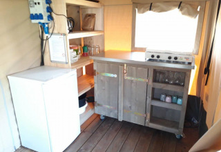 Et lille køkkenhjørne med komfur, køleskab og åbne hylder i Safari tent Merel på Camping De Gouwe Stek.