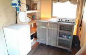Kleine kitchenette met fornuis, koelkast en open schappen in Safari tent Merel op Camping De Gouwe Stek.