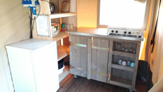 Piccolo angolo cottura con fornello, frigo e scaffali nella Safari tent Merel al Camping De Gouwe Stek.