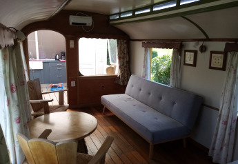 Interior del lodge Glamping Pipowagen Klukkluk con sofá, mesa y sillas en Camping De Gouwe Stek.