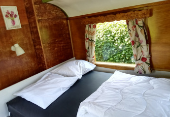 Dormitorio en Glamping Pipowagen Klukkluk con cama doble, cortinas florales y vista natural en los Países Bajos.