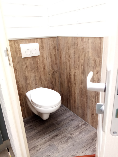 Baño moderno con inodoro suspendido y paneles de madera en Glamping Pipowagen Klukkluk, Países Bajos.