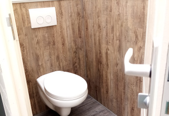 Baño moderno con inodoro suspendido y paneles de madera en Glamping Pipowagen Klukkluk, Países Bajos.