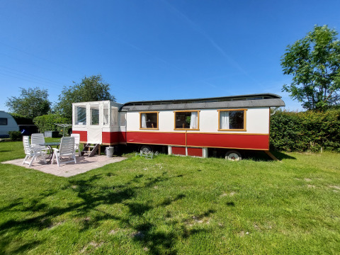 Afbeelding van Glamping Pipowagen Klukkluk met tuinmeubilair op een grasveld onder een blauwe lucht.