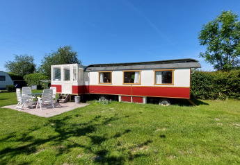 Foto del Glamping Pipowagen Klukkluk, con área para sentarse al aire libre sobre césped y cielo azul claro.