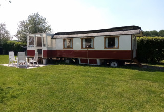 Glamping Pipowagen Klukkluk en Camping De Gouwe Stek, Países Bajos, con mesa y sillas de jardín al frente.